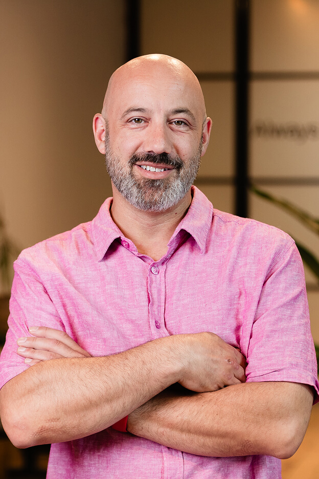 Team member at Always Beyond Calgary IT services wearing a pink shirt with arms crossed in office setting.